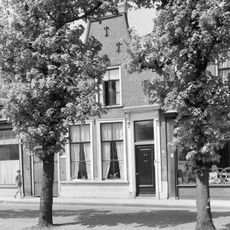 Woonhuis onder zadeldak tegen halsgevel met aanzetkrullen en bekroond door fronton