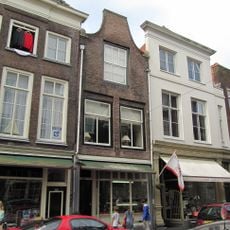 Pand met eenvoudige tuitgevel met rollaag, eindigend in natuurstenen voluten op geprofileerde dekplaten en bekroond door een rechte lijst