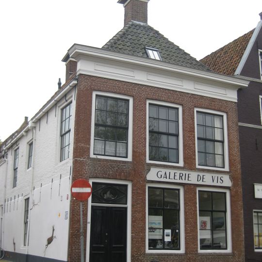 Pand met gevel met rechte kroonlijst met compartimenten onder schilddak met voorschild met twee topschoorstenen met bord