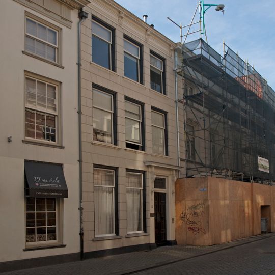 Huis met sobere gepleisterde lijstgevel. Ingangspartij met voluutvormige consoles onder kroonlijstje