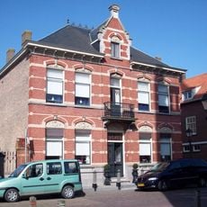 Herenhuis, gebouwd in eclectische stijl met natuurstenen stoep, stoeppalen en ten zuiden aan de voorgevel een ijzeren hekwerk tussen rode bakstenen kolommen