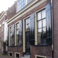 Eenvoudig laag huis met rechte kroonlijst. Brede bakstenen gevel. Gevelsteen met de Franse lelie