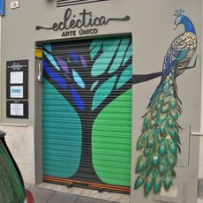 Mural que representa un pavo real posado con la cola recogida sobre la rama de un arbol.