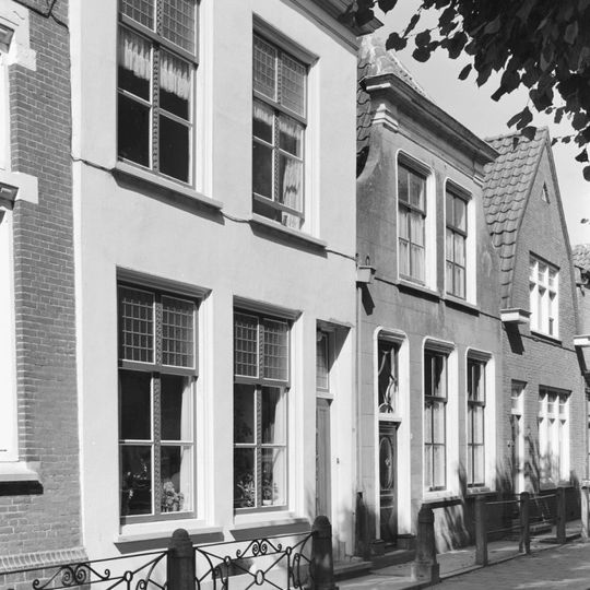 Huis met gepleisterde lijstgevel met ingezwenkte top, voordeur- en vensteromlijstingen met afgeronde hoeken. Voordeur met na-empire velden.