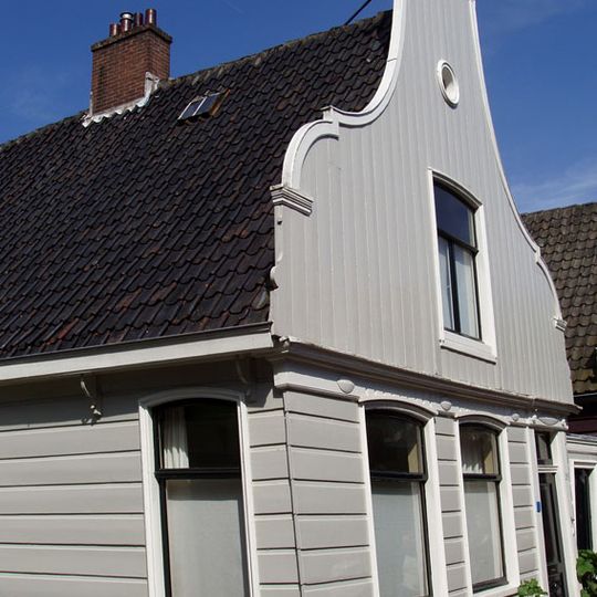 Houten dijkhuis met klokgevel uit 19de eeuw, onderpui in empire-stijl