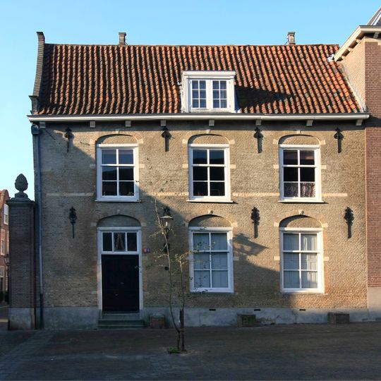 Pand zonder verdieping, zonder zadeldak, dat aansluit tegen een puntgevel met vlechtingen en oeil-de-boeuf in gebeeldhouwde omlijsting