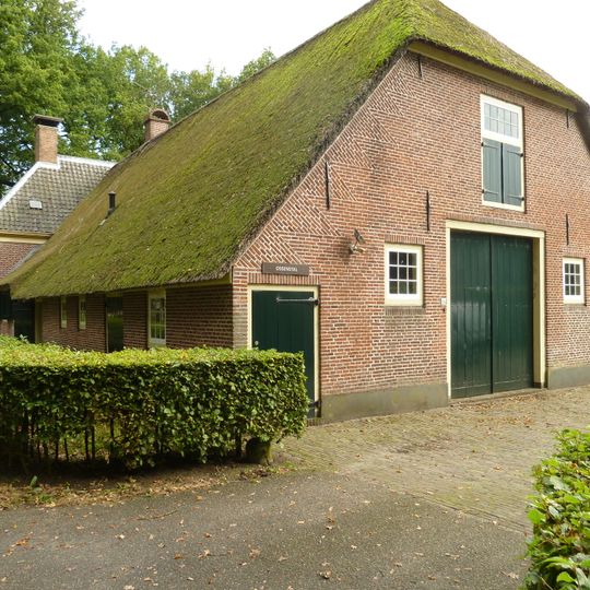 Boerderij waarvan het woonhuis dwars voor de stal is gebouwd en een pannen schilddak met hoekschoorstenen draagt