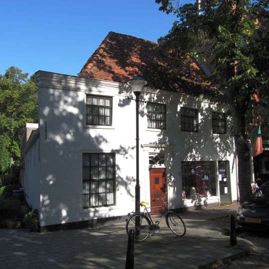 Gepleisterd pand voorgedeelte evenwijdig aan de straat, onder hoog schilddak.