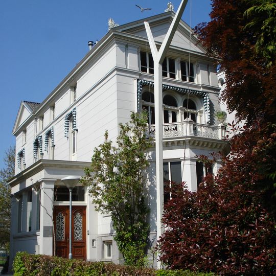 Villa. Gepleisterde gevel met getoogde en rechthoekige vensters, driezijdig uitgebouwde erker met balconhek en bekronend fronton