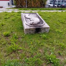 Steinrelief mit Fischmotiv im Grasbereich beim Gewerbegebiet