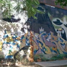 Grafiti acompañado de varios elementos figurativos: un templo maya, un tucán, una serpiente y unos platillos volantes.