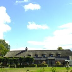 Brabantse langgevelboerderij. Schilddak met riet en pannen gedekt. In het woongedeelte vensters met luiken en 25-ruitsschuiframen. In de stal een zijbaander