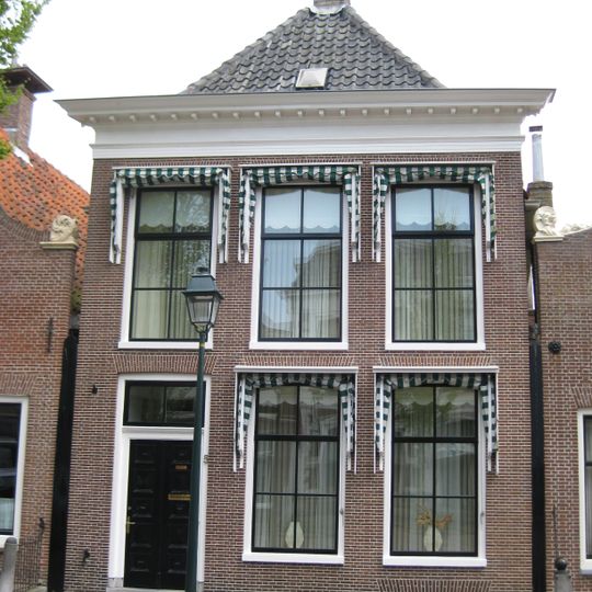 Pand met versierde rechte kroonlijst onder schilddak met hoekschoorstenen