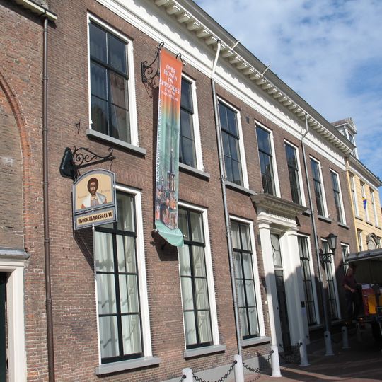 Pand op natuurstenen plint met brede lijstgevel met modillons