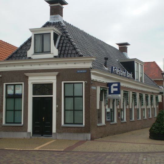 Diep pand met omlijste ingang en versierde kroonlijst onder voor- en achter afgeschuind zadeldak met twee dakkapellen en schoorstenen boven voor- en achterschild