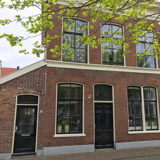 Aan voorzijde verbreed pand met rechte kroonlijst onder zadeldak met topschoorsteen met bord