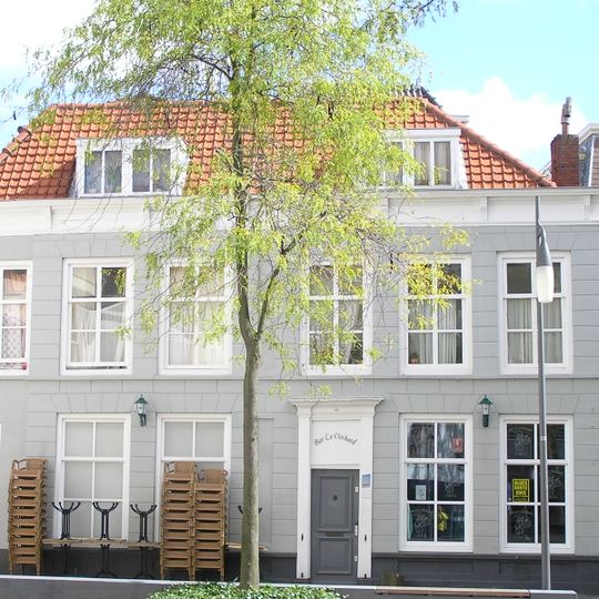 Breed hoekpand met gepleisterde rechte gevel aan de Vlasmarkt. Waarschijnlijk bestaande uit enige in de kern oudere panden, samengevoegd achter een 19e of begin 20e eeuw gevel in traditionele trant