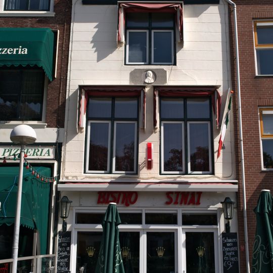 Huis met gepleisterde gevel. Eenvoudige voordeuromlijsting met rozetbovenlicht. Gevelsteen met buste van Jacobus Bellamy