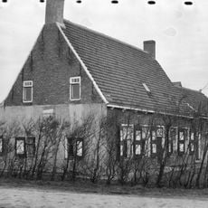 Boerderij. Bakstenen woonhuis met pannen zadeldak. Gepleisterde onderzijde van topgevel. Bakgoot op klossen ramen met 2 paneelblinden en rollagen boven ramen.