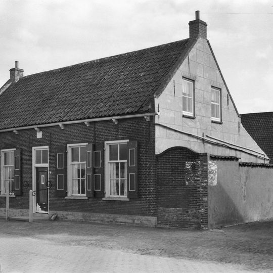 Huis onder zadeldak met langsgevel aan de Ring. Stoeppalen met krulijzers aan de gevel verbonden