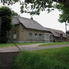 Boerderij met links een onderkelderde opkamer, waarin vensters met middenstijlen en luikjes. Keldervensters in getoogde omlijstingen. Rieten wolfdak