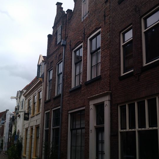 Pand met bakstenen topgevel met in en uitgezwenkte contouren, gemetselde, vierkante pinakels en geprofileerde waterlijsten. Gerestaureerd 1953