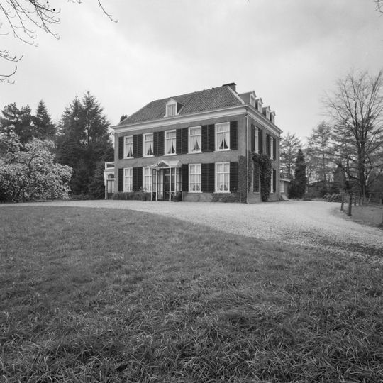 In park gelegen herenhuis met verdieping en omlopend schilddak. Deur met bovenlicht en in de parterre vensters met zesruitsschuiframen