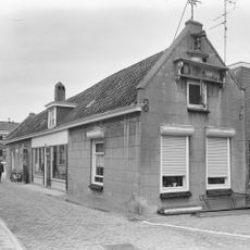 Pand beschermd vanwege smeedijzeren gevelbekroning in de vorm van een gestileerd kruis met in de top als windvaan een ruiter