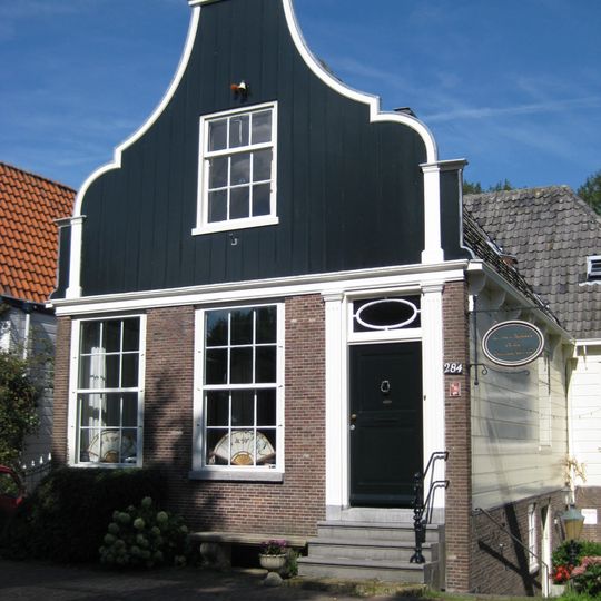 Houten dijkhuis met klokgevel uit 19de eeuw en met bakstenen onderpui