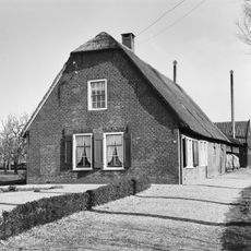Boerderij, onder rieten wolfdak. Voorgevel met vlechtingen en vensters met luiken en 6- en 12-ruitsschuiframen