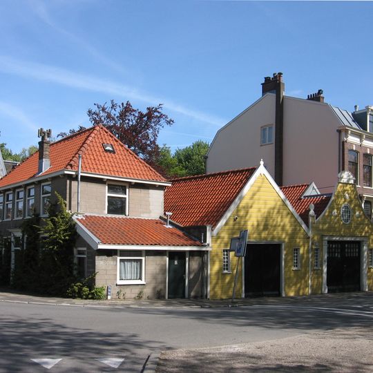 Langgerekte houten schuur onder zadeldak en eenvoudige geverfde puntgevel. Met inrijpoort