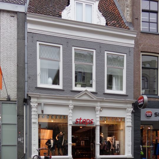 Huis met jongere winkelpui in lijstgevel onder dwars zadeldak mer versierde dakkapel