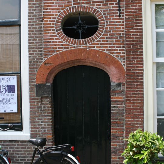 Poortje. Geprofileerd gemetseld rondboogpoortje van geslepen steen. Boven poortje ovaal venster met smeedwerk