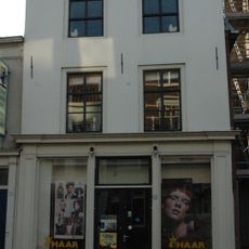 Hoekpand (naast R.K.Kerk). Pand met schilddak, aan de achterzijde afgesloten door een puntgevel. Gepleisterde lijstgevel met schuiframen in de verdiepingen. Zijgevel modern