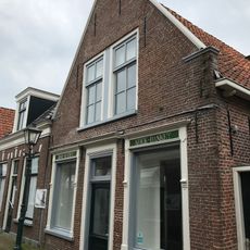 Woning onder zadeldak tegen topgevel met omlijste ingang en vensters en met vlechtingen langs de zijden en opgaand van aanzettreden