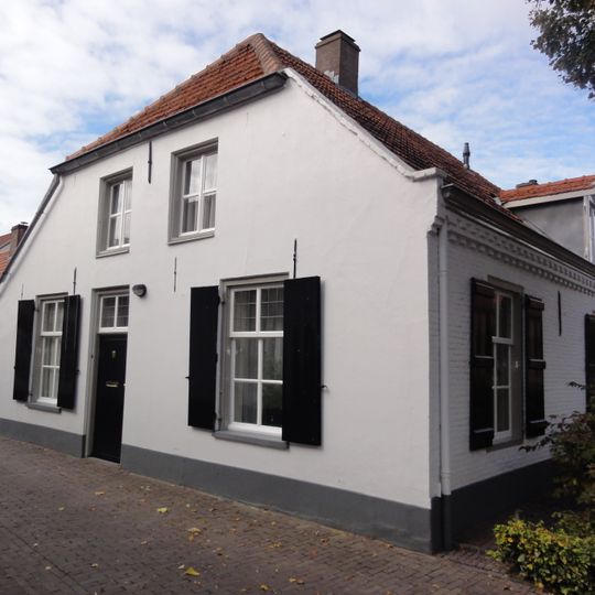 Wit dorpshuis met rood pannendak, langsgevel aan de Gasthuisstraat, korte gevel met wolfdak aan de Dekanijstraat