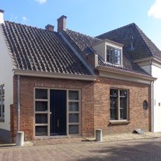 Witgepleisterd huis met verdieping en hoog schilddak, belangrijk door zijn ligging aan de Linge bij de toegang tot het dorp