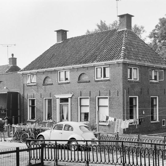 Pand met omlijste ingang en verdieping onder schilddak met hoekschoorstenen en gedichte halfronde lichtopeningen