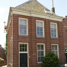Huis onder schilddak en met lijstgevel, ingedeeld door een middenrisaliet en bakstenen geblokte pilasters