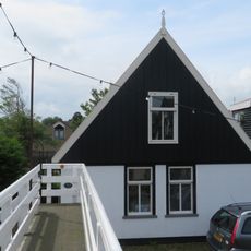 Pand onder zadeldak. Gepleisterde gevel waarboven houten geveltop