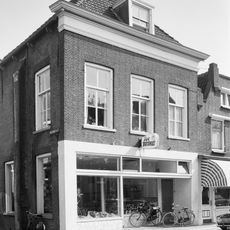 Markant hoekpand met verdieping en schilddak. Eenvoudige lijstgevel, waarin vensters met zesruitsschuiframen