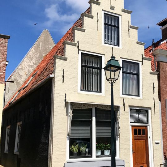 Pand onder zadeldak tegen gepleisterde trapgevel met verhoogd achterhuis tussen twee puntgevels