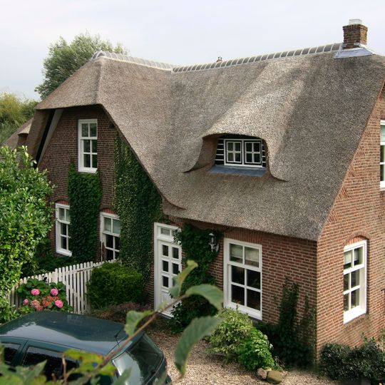 Boerderij met dwars woongedeelte onder rieten wolfdak. Het middendeel van de gepleisterde voorgevel is verhoogd tot een puntgevel. Vensters met zesruitsschuiframen en luiken