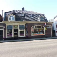 Verdiepingloos pand onder mansarde dak; daterend uit de bouwtijd van de kerk en in een verband daarmee aangelegd