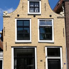 Smal pand onder zadeldak tegen ingezwenkte halsgevel met aanzetkrullen en bekronend fronton