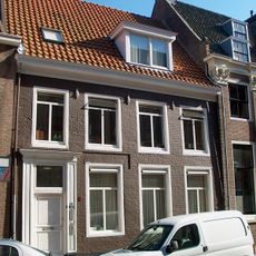 Gevel met omlijste ingang voor ouder pand met dwarskap tussen topgevels