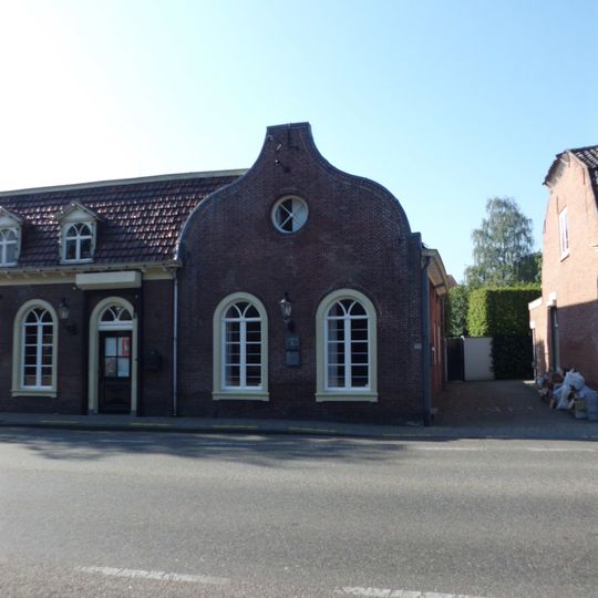 Verdiepingloos pand onder zadeldak; daterend uit de bouwtijd van de kerk, en in een verband daarmee aangelegd