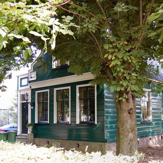 Houten huis met aan de straat een ingezwenkte voorschot met fronton, gesneden lijsten en zijmeanders met rozetten