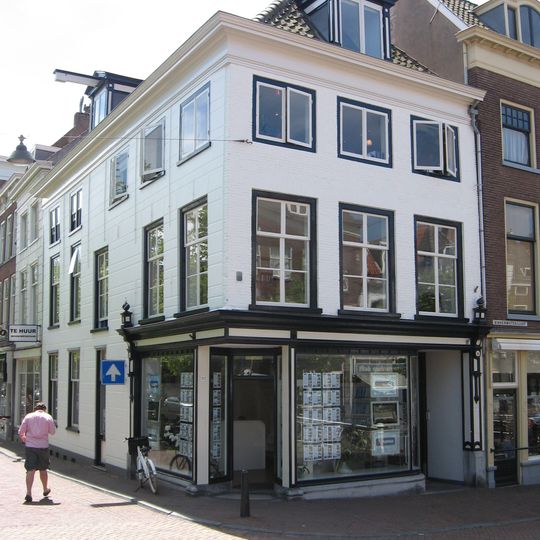 Hoekpand Oude Delft. Pand ter diepte van zes assen, parterre en twee verdiepingen, schilddak. Eenvoudige voorgevel met lage bovenverdieping en kroonlijst