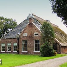 Kop-rompboerderij met asymmetrisch geplaatst voorhuis onder pannen zadeldak met schoorsteen met bord